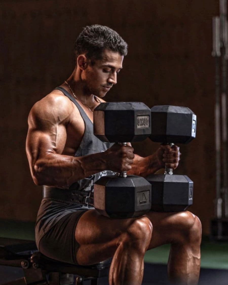 Alex Djurovic seated on a bench holding dumbbells mid-set